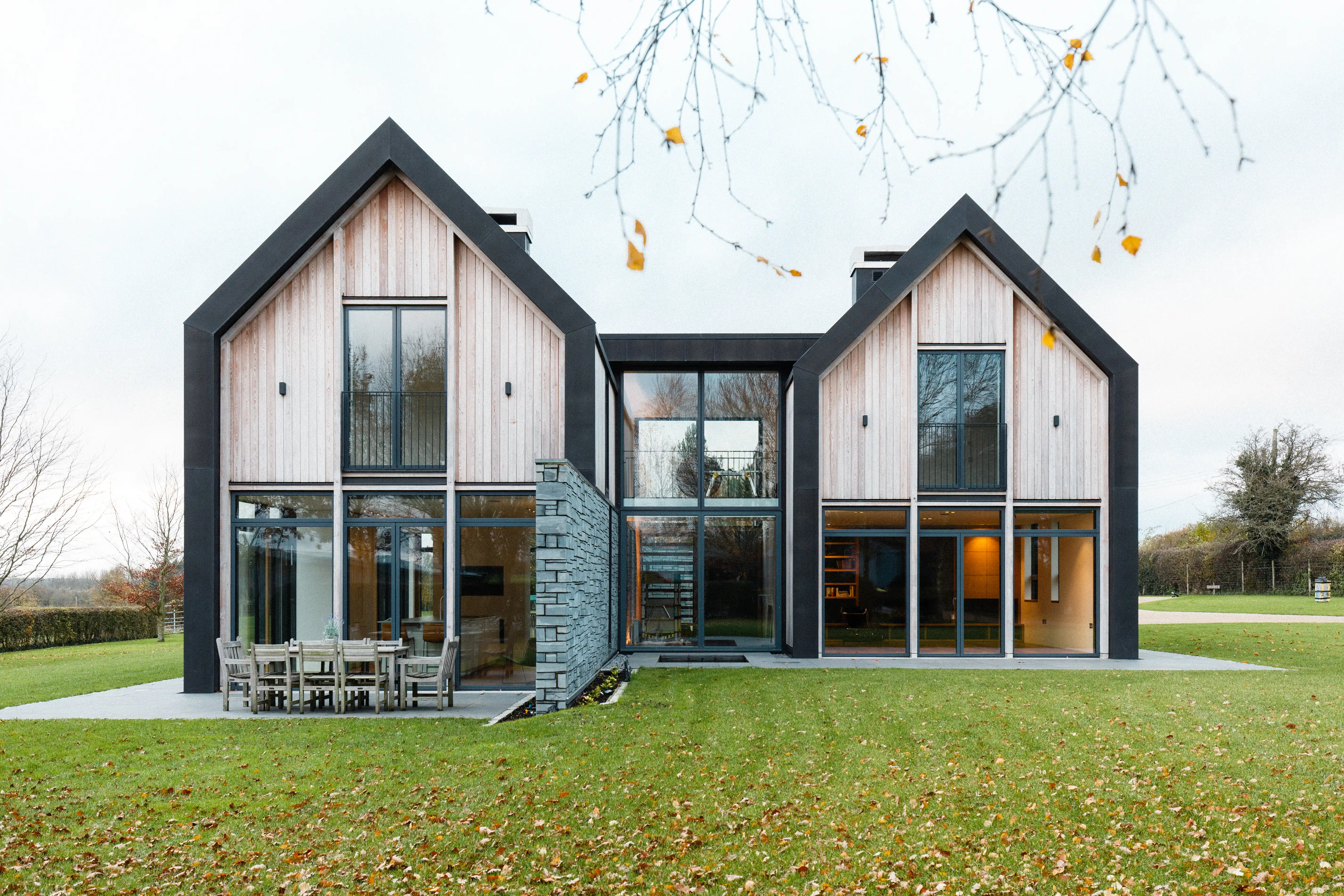 The garden elevation, two timber-clad gables linked by a glazed bay, with a stone wall and terrace