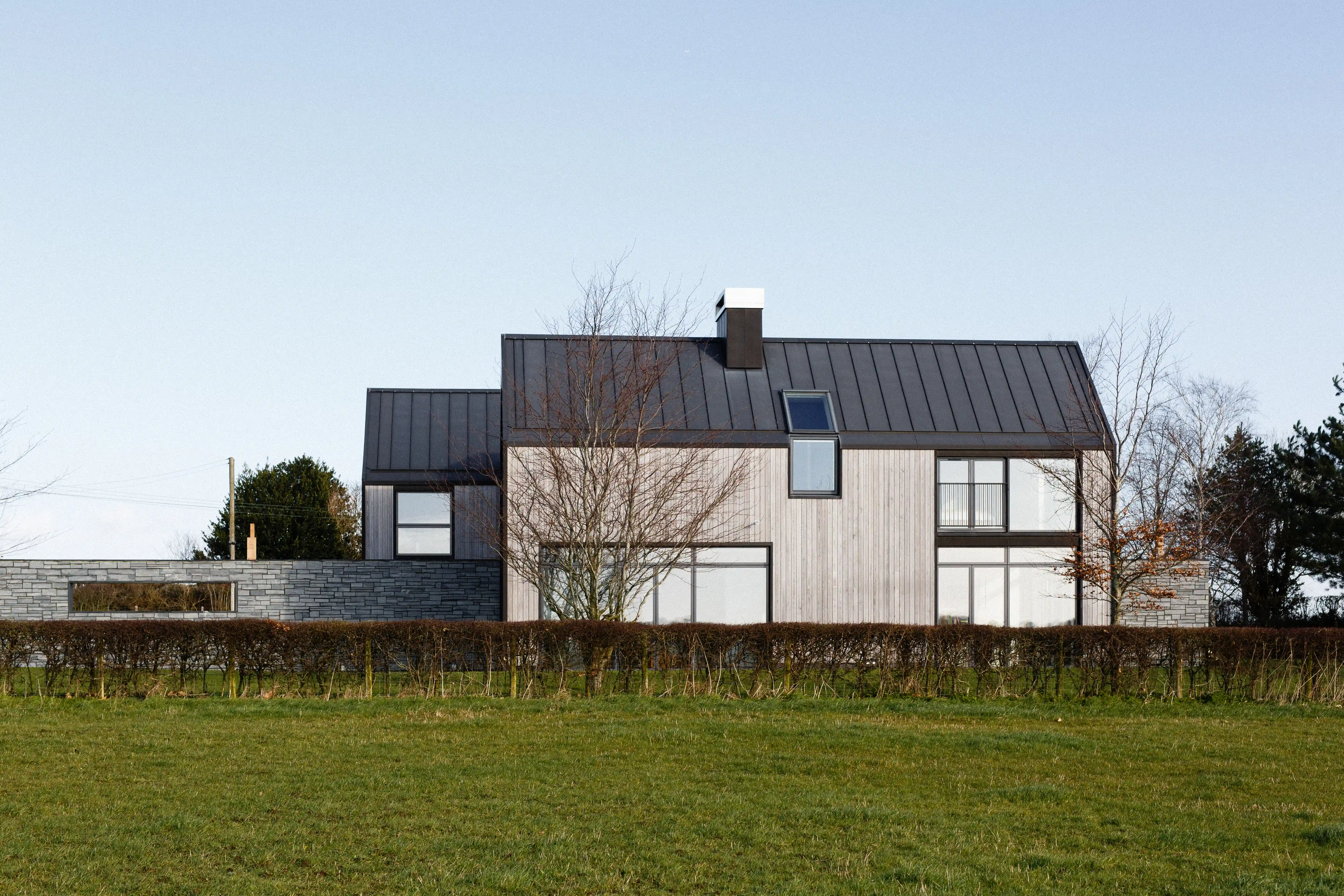The house seen across the field, with its standing seam metal roof, timber cladding and stone boundary wall