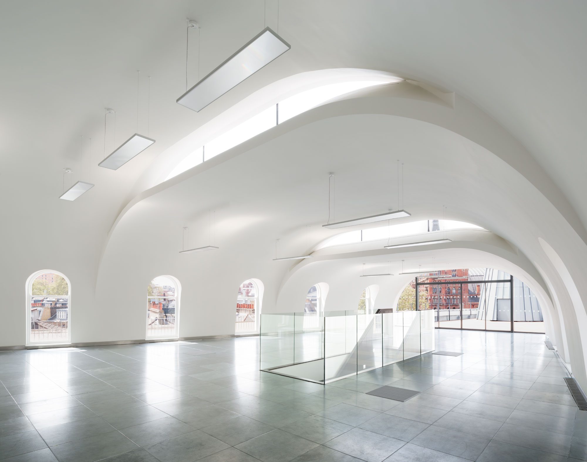 Top-floor interior beneath white vaulted ceilings, with arched windows and a glass balustrade around the stair opening