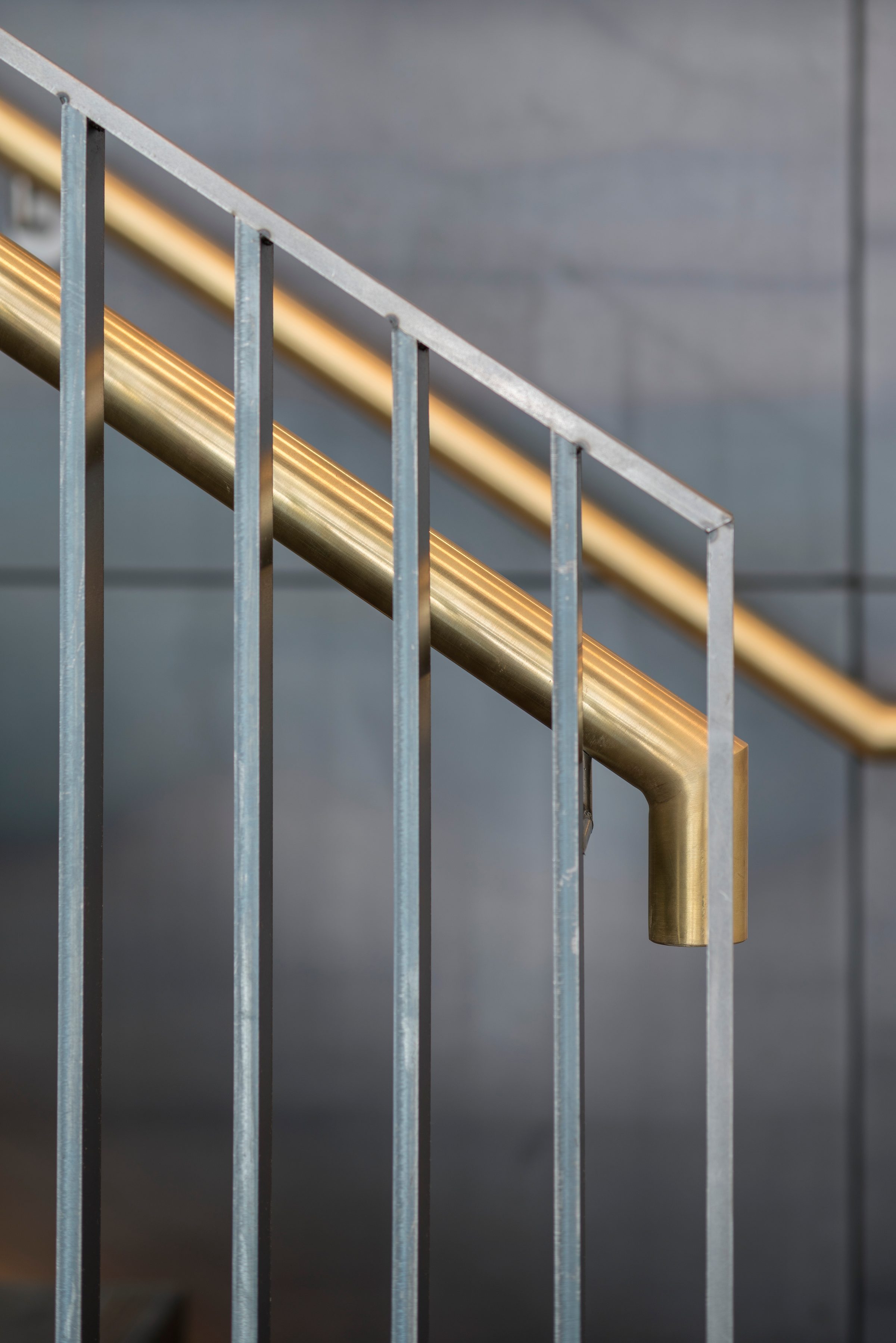 Detail of the brass handrail and galvanised steel balusters against the dark metal stair wall
