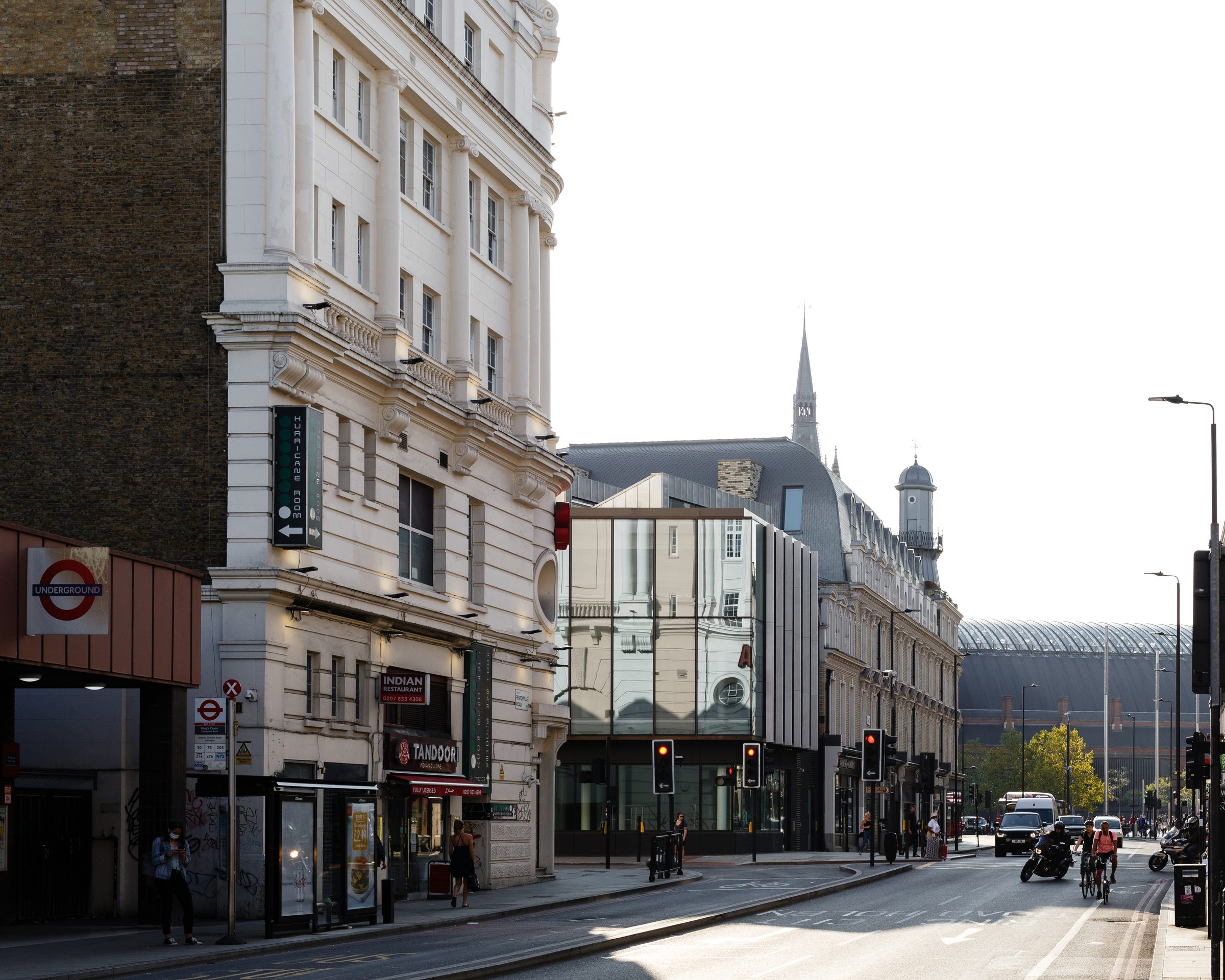 The building seen along the street, its glazed frontage set among older facades near the station