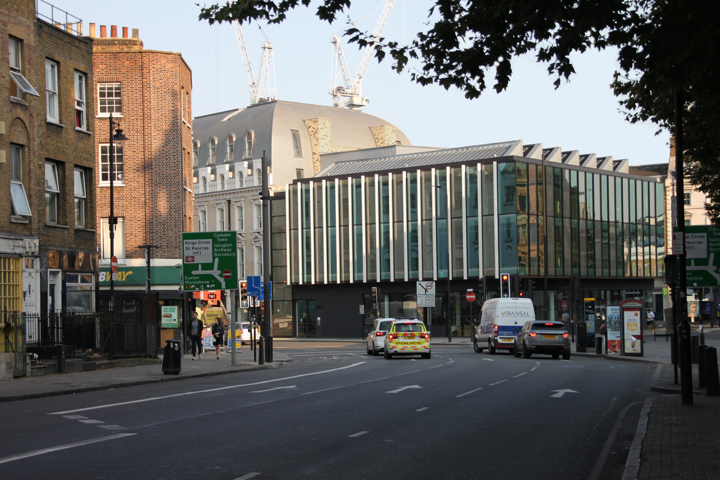The sawtooth glazed roof and upper floors seen from the street, with construction cranes beyond