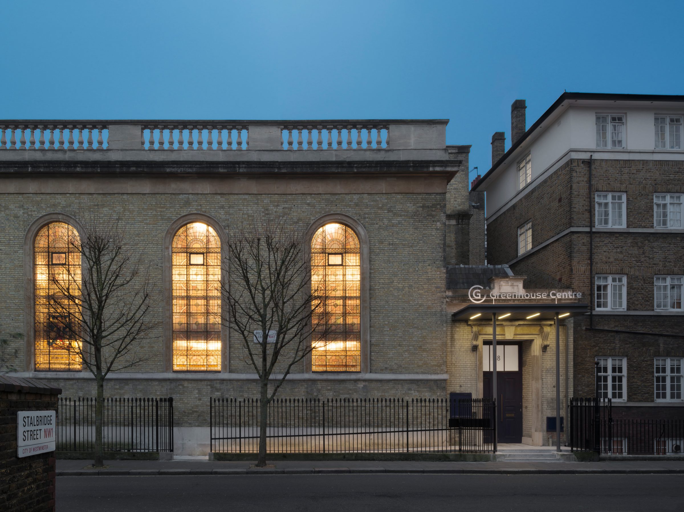 The lit arched windows and new entrance canopy seen from across the street at dusk