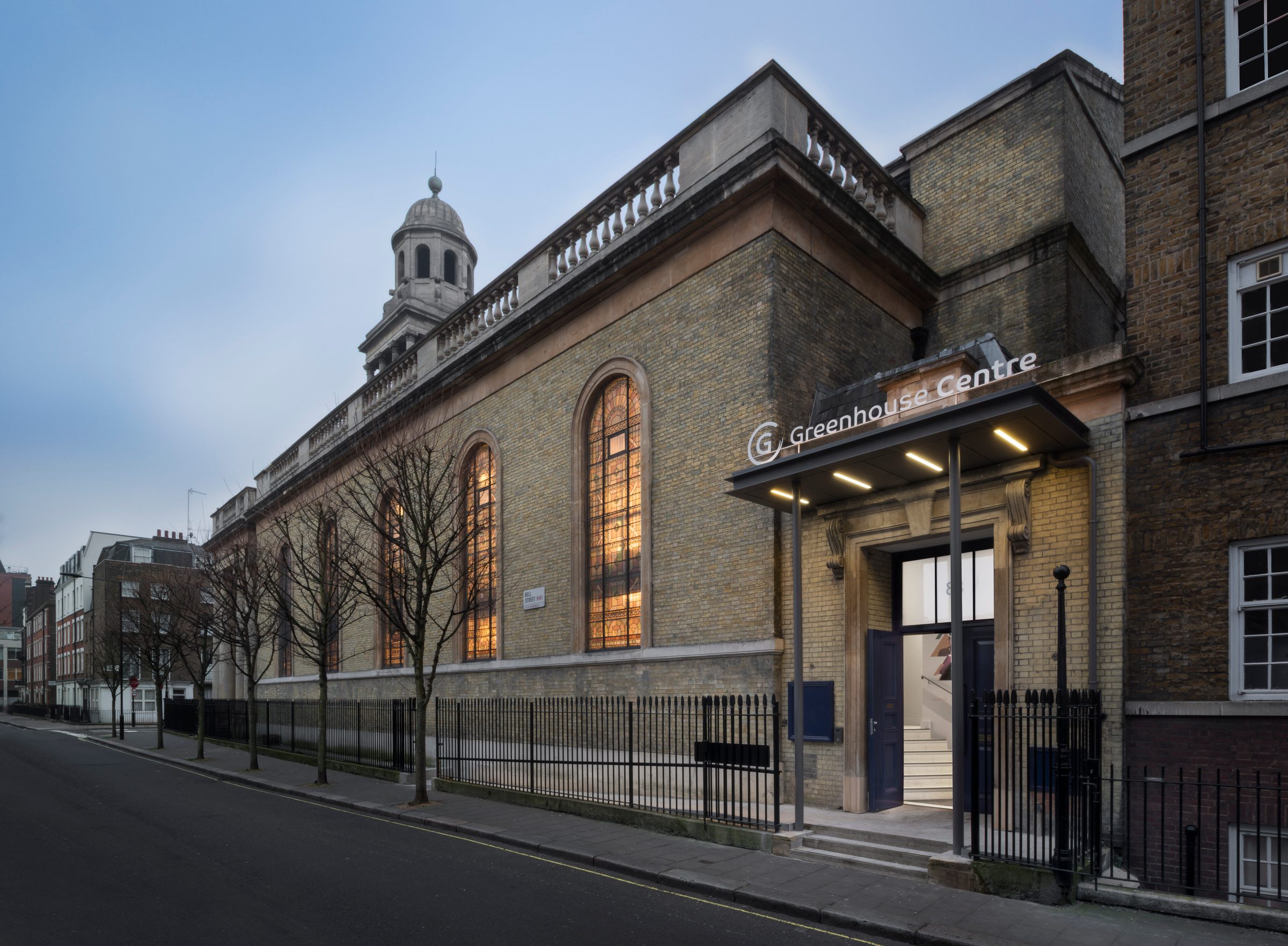 The Greenhouse Centre entrance at dusk, with the arched windows of the hall lit along the flank wall