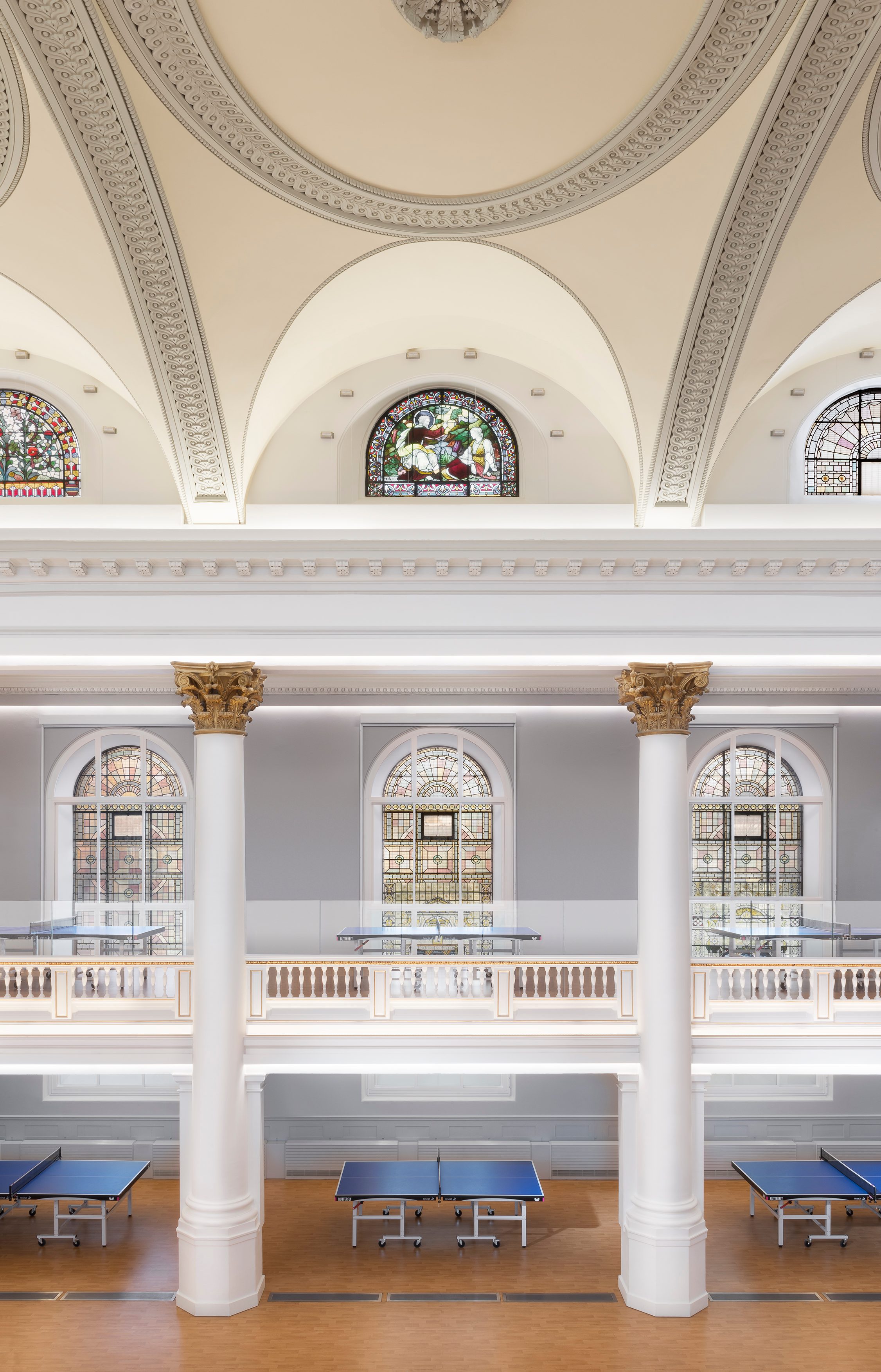 Stained glass windows and restored plasterwork at gallery level, with the vaulted ceiling above