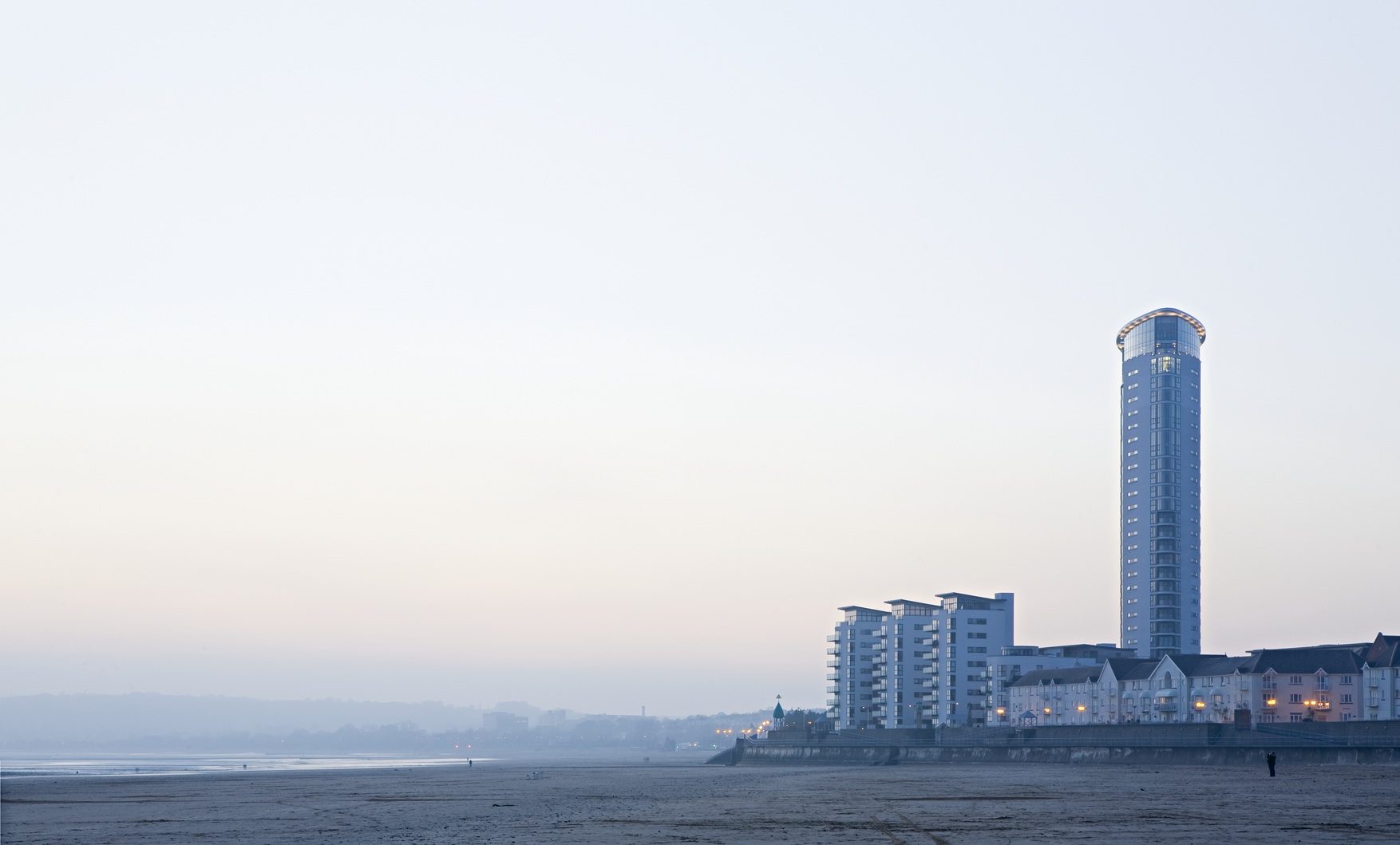 The tower seen across the beach at first light, with the lower apartment blocks along the seafront