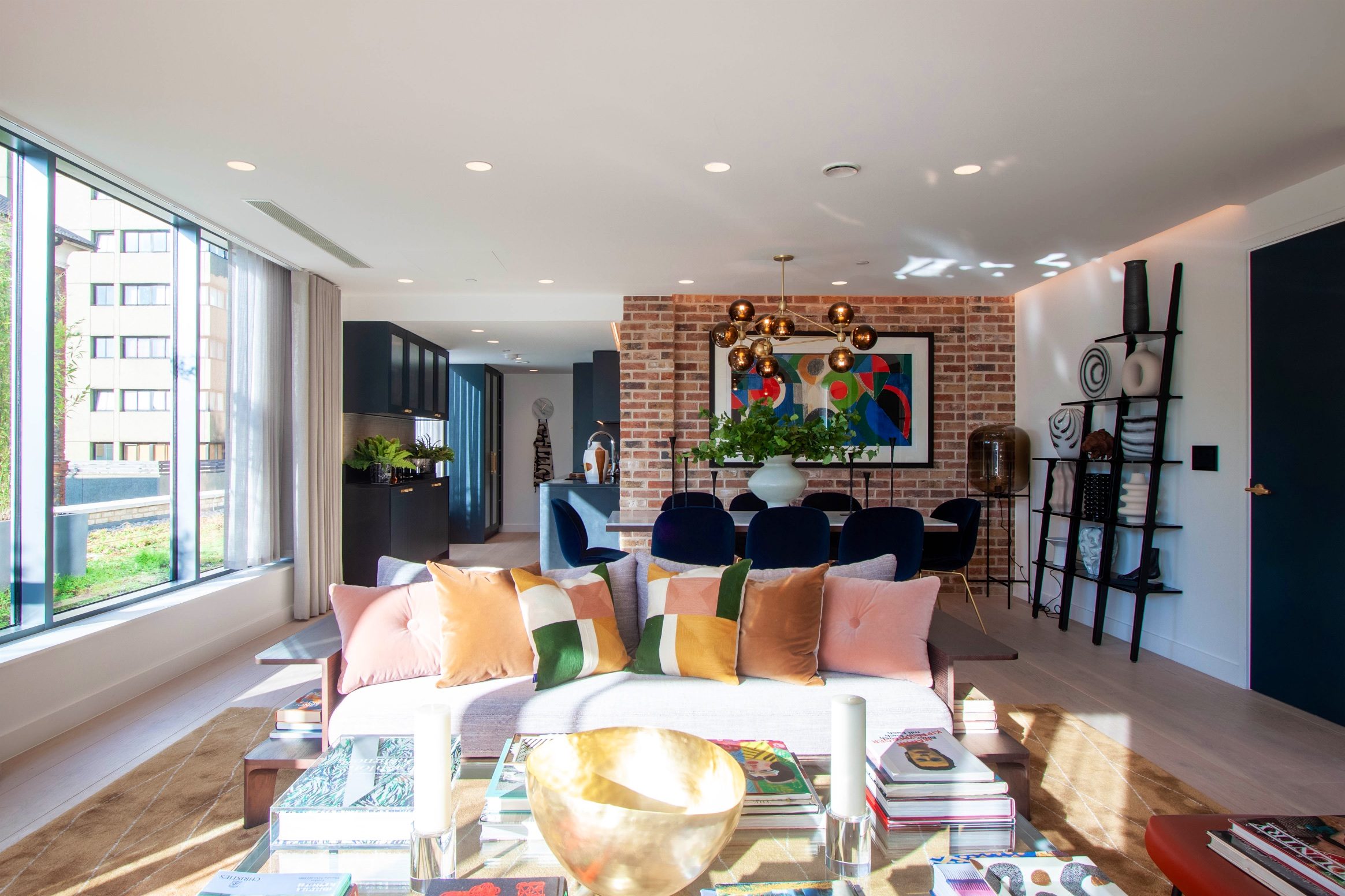 Open-plan living and dining space with an exposed brick wall and copper pendant lights