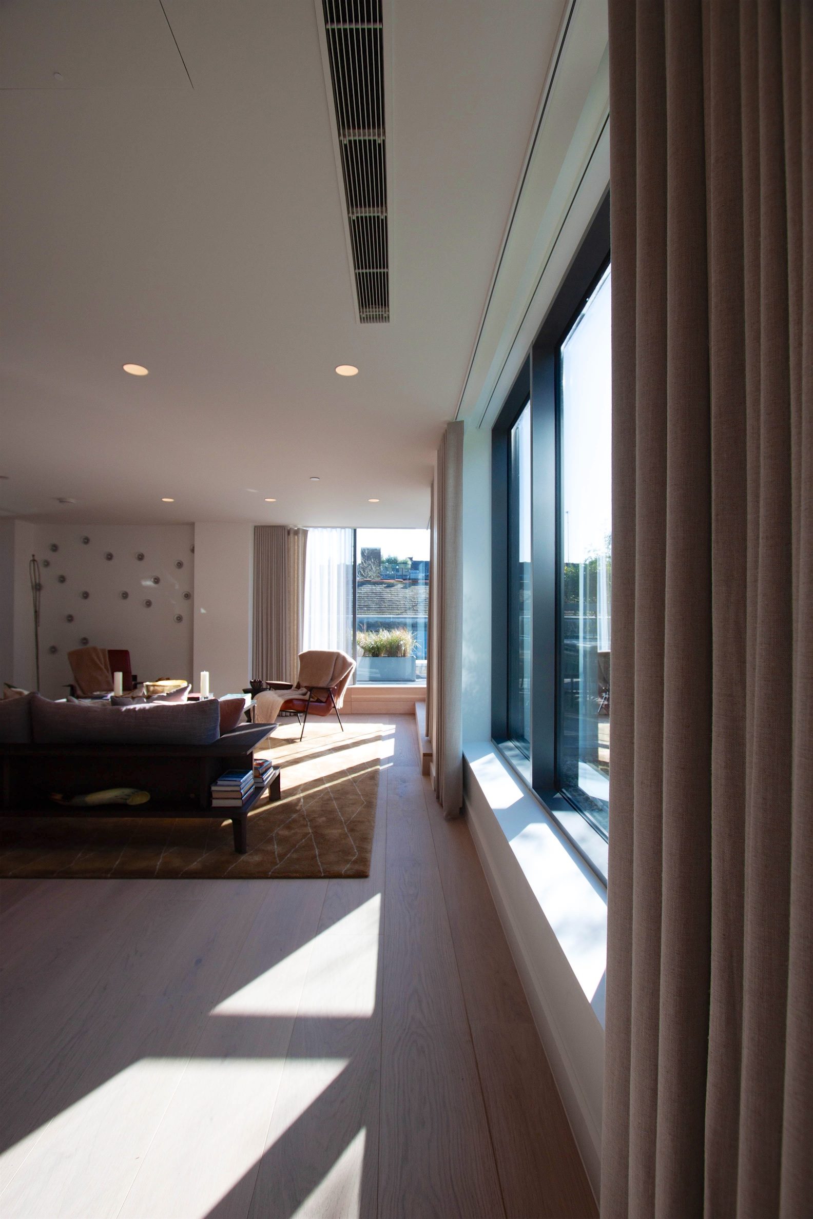 Living room with full-height glazing and oak flooring, sunlight falling across the room