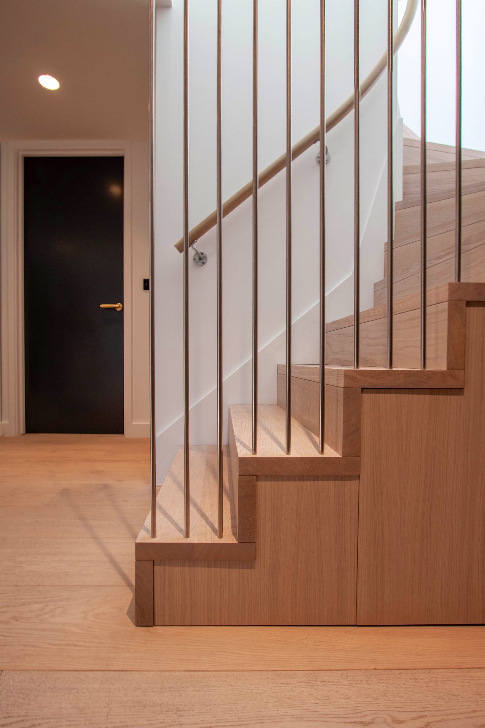 Oak stair with slender metal balusters and a timber handrail, rising from the oak-boarded hall