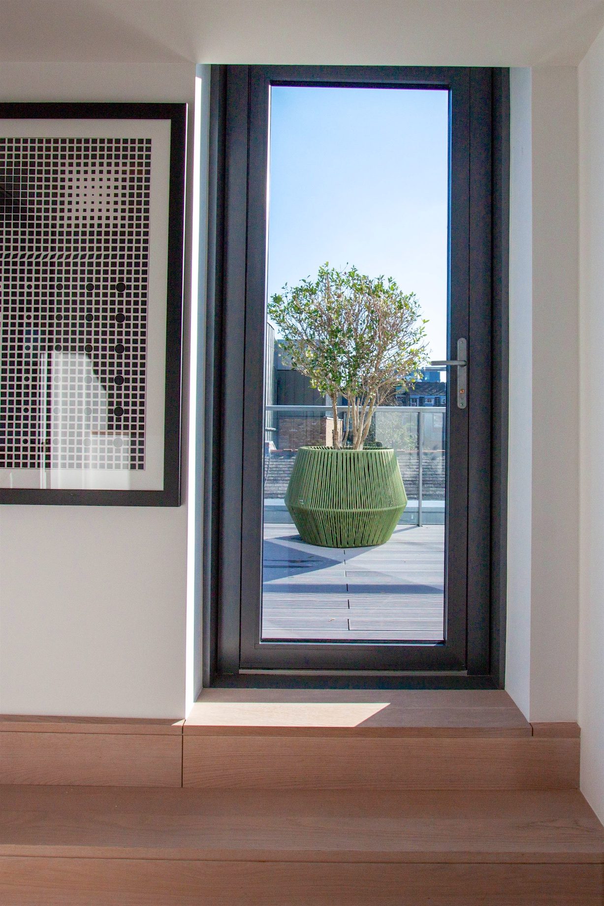 View through the terrace door to a ribbed green planter and small tree on the decking