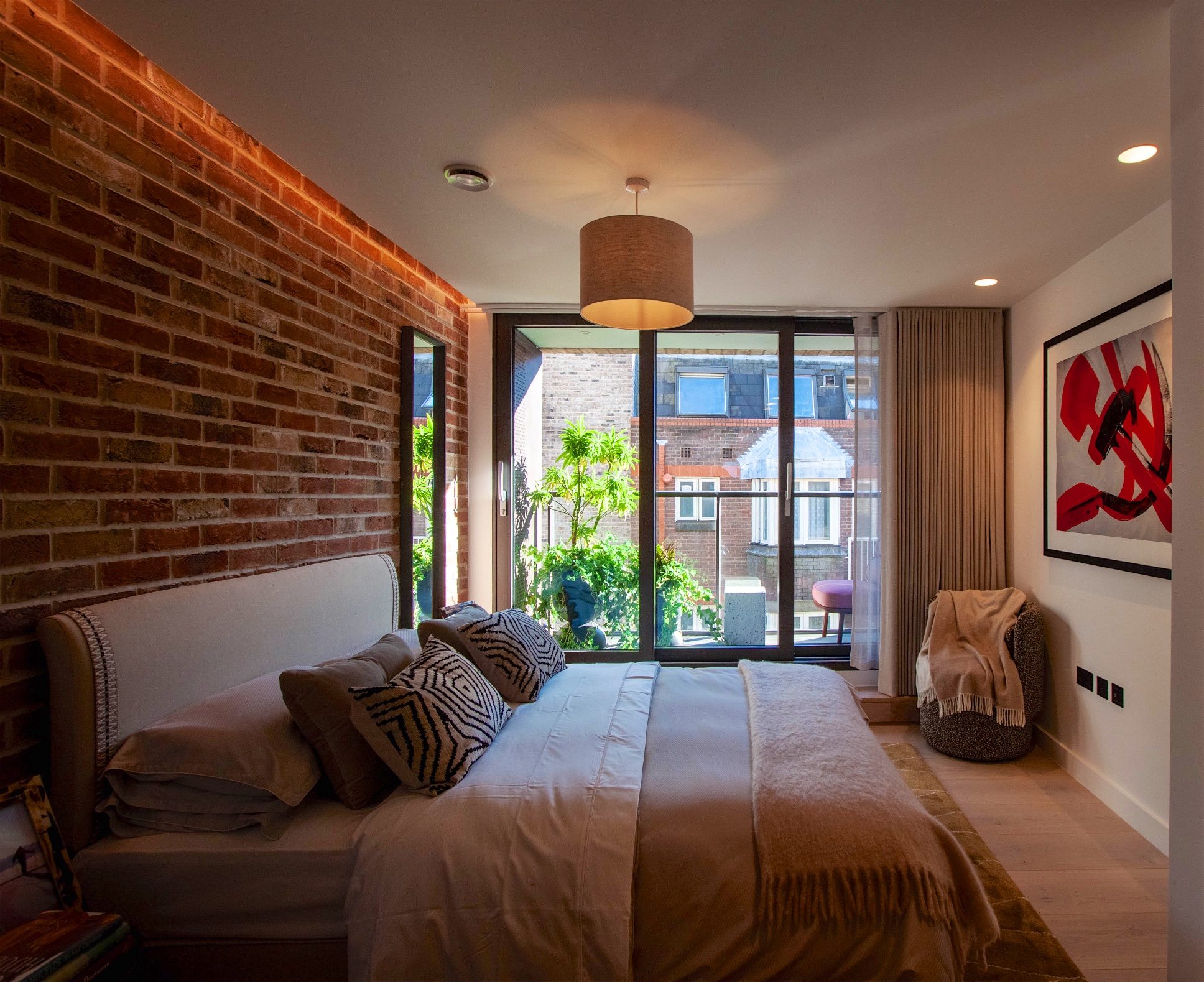 Bedroom with an exposed brick wall and a glazed door onto a planted balcony above the rooftops
