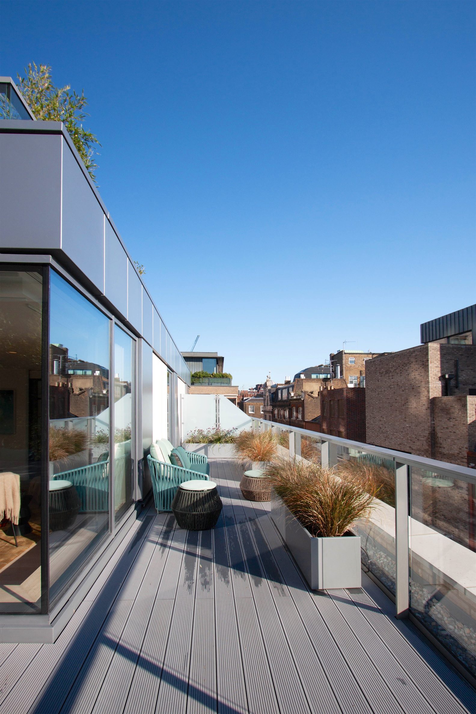 Roof terrace with timber decking, planted grasses and a glass balustrade, looking out over the Soho rooftops