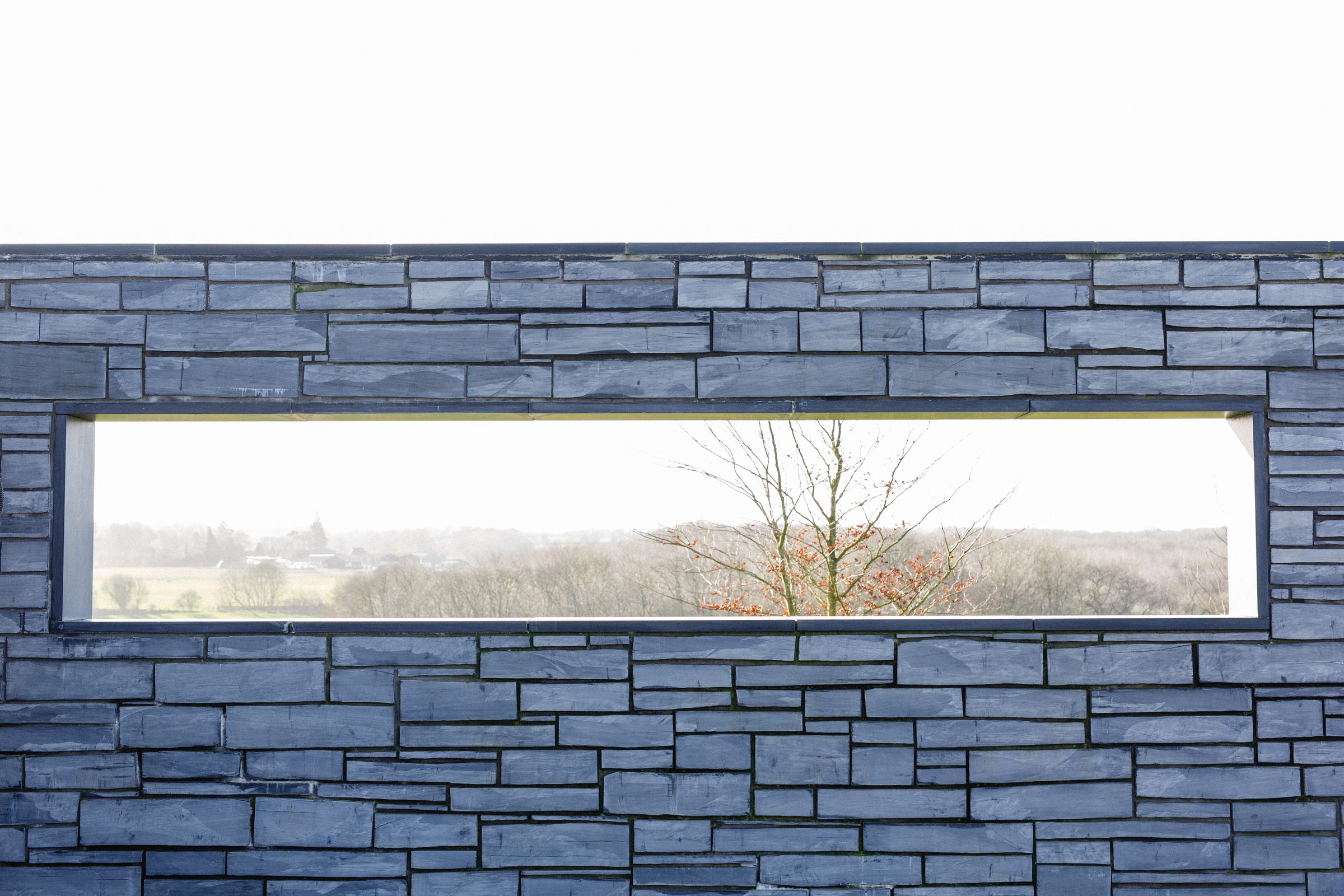 A long slot window set into the slate wall, framing a view of the landscape beyond