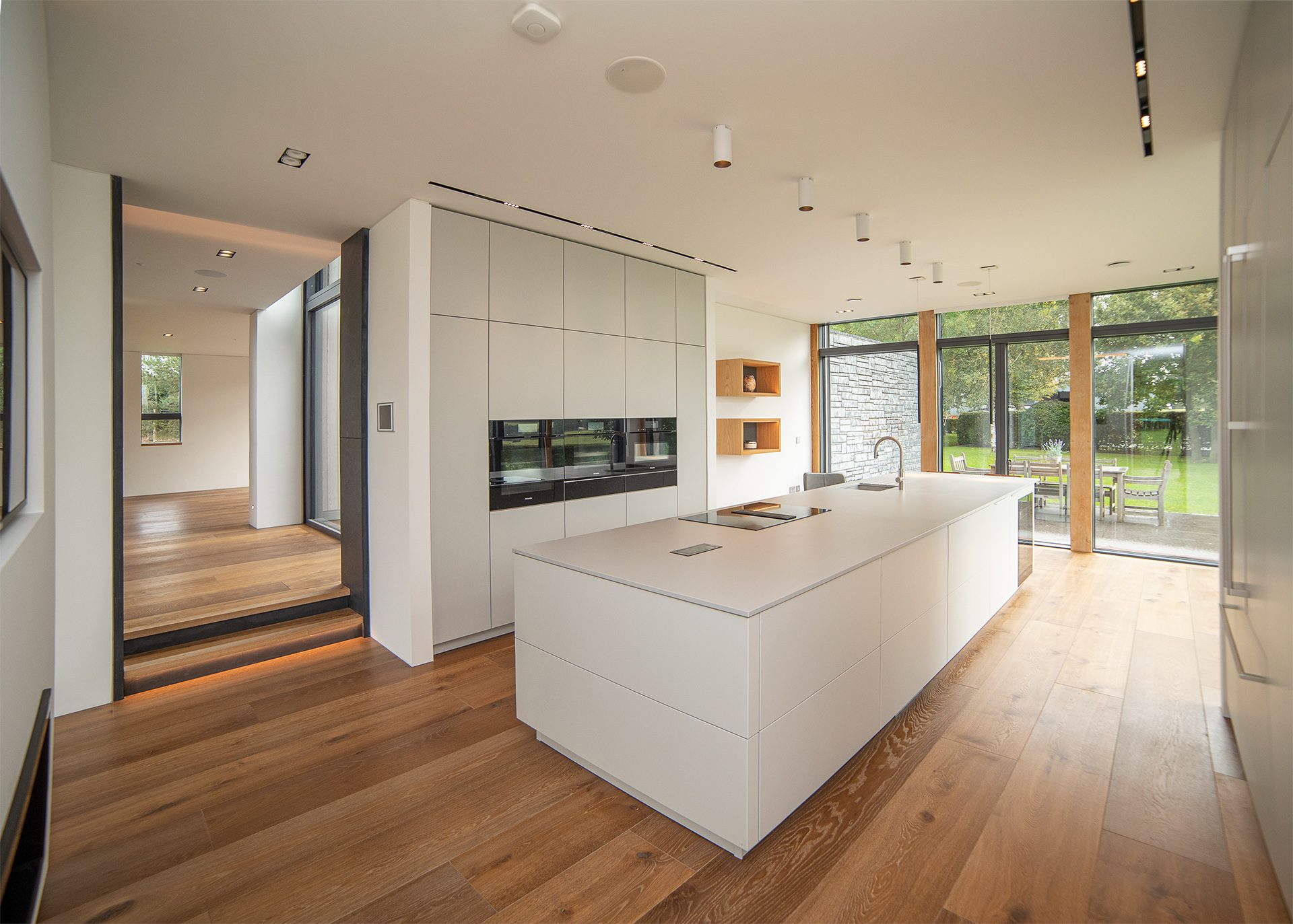 Kitchen with a white island and full-height glazing onto the garden, oak boards throughout