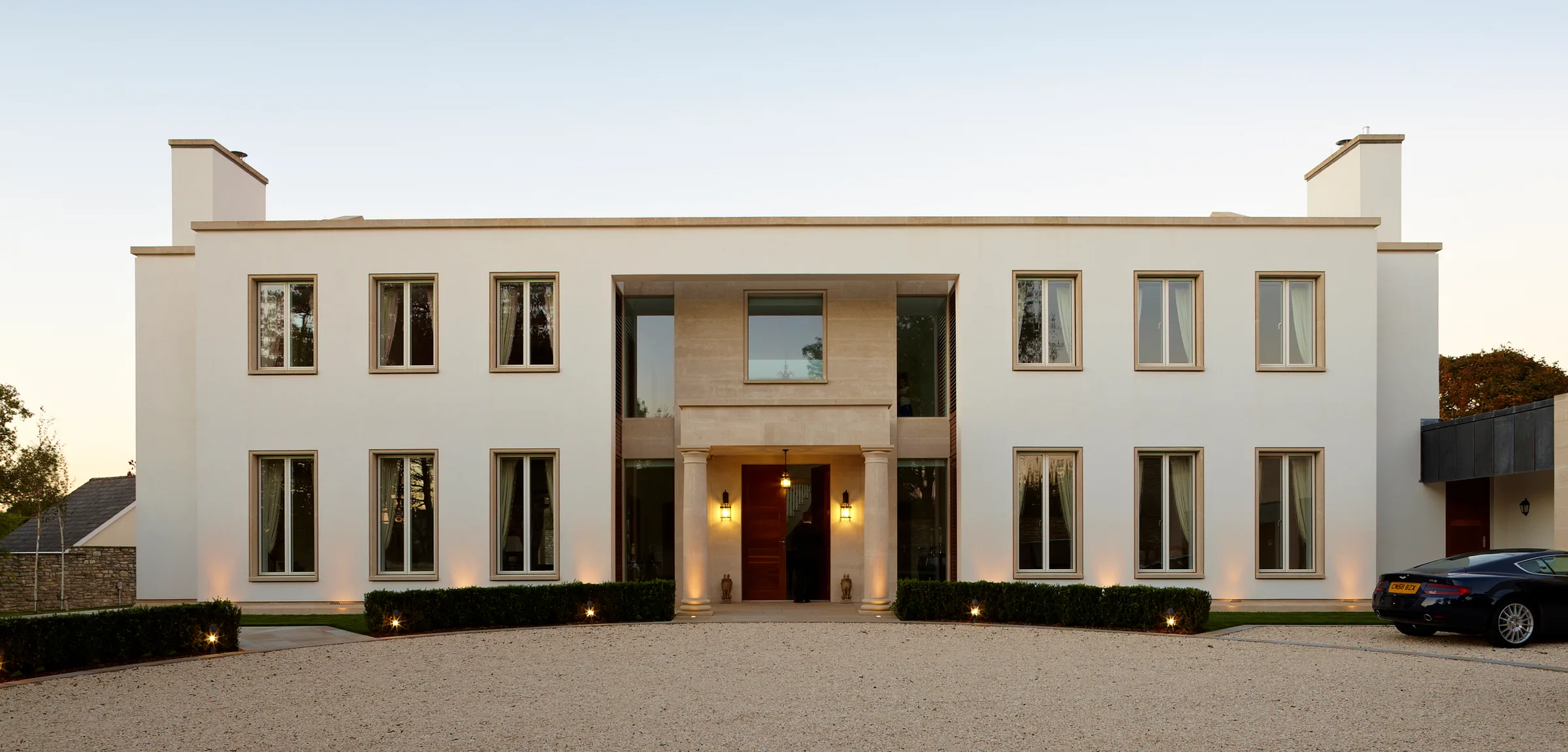 The entrance front at dusk, with its stone doorcase, clipped hedges and gravel forecourt