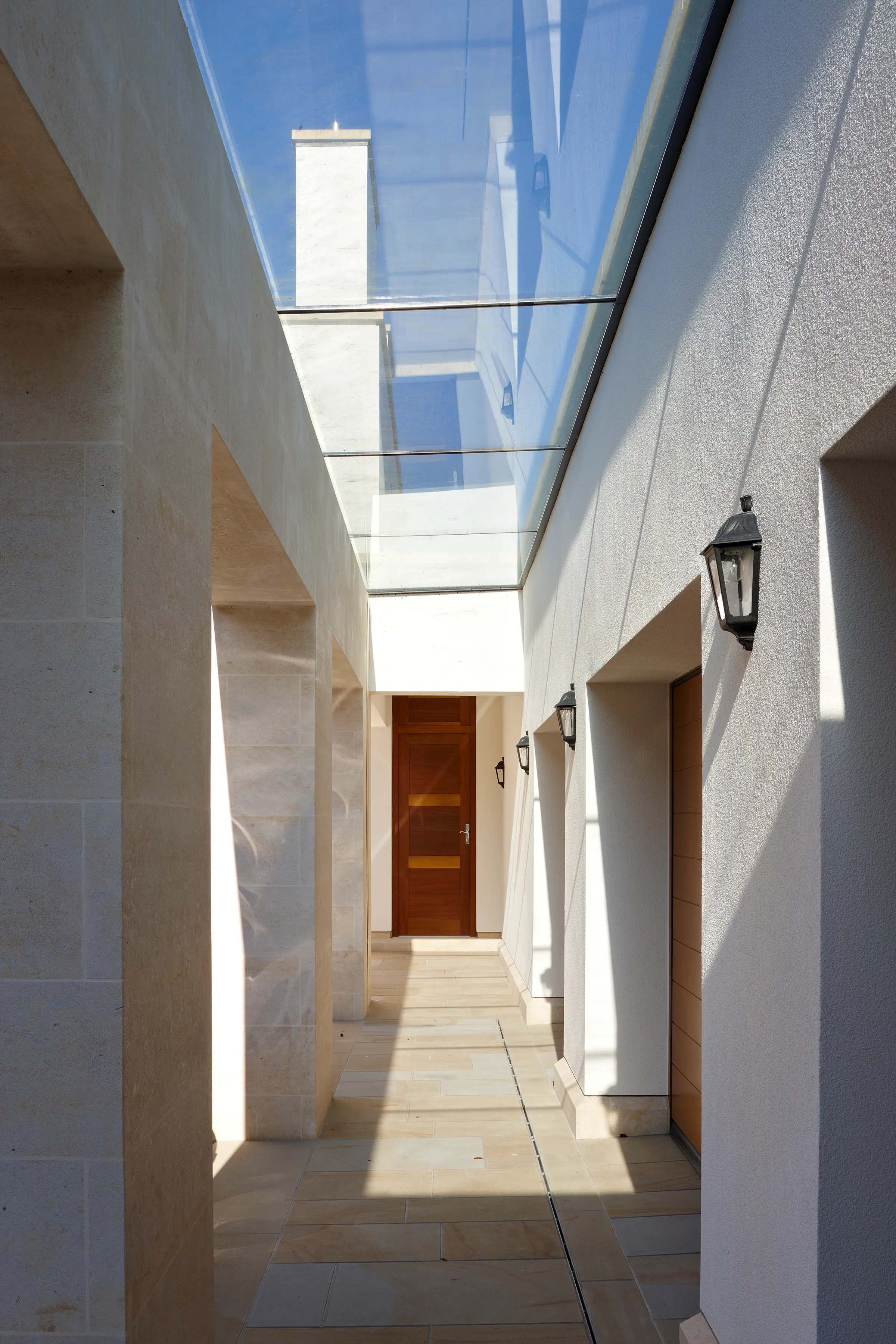 Glass-roofed courtyard passage with stone paving and rendered walls, leading to a timber door