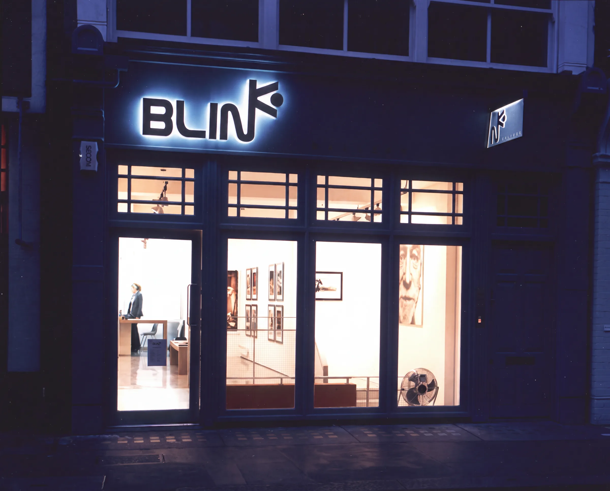 The gallery shopfront lit at night, with the illuminated sign above the glazed frontage
