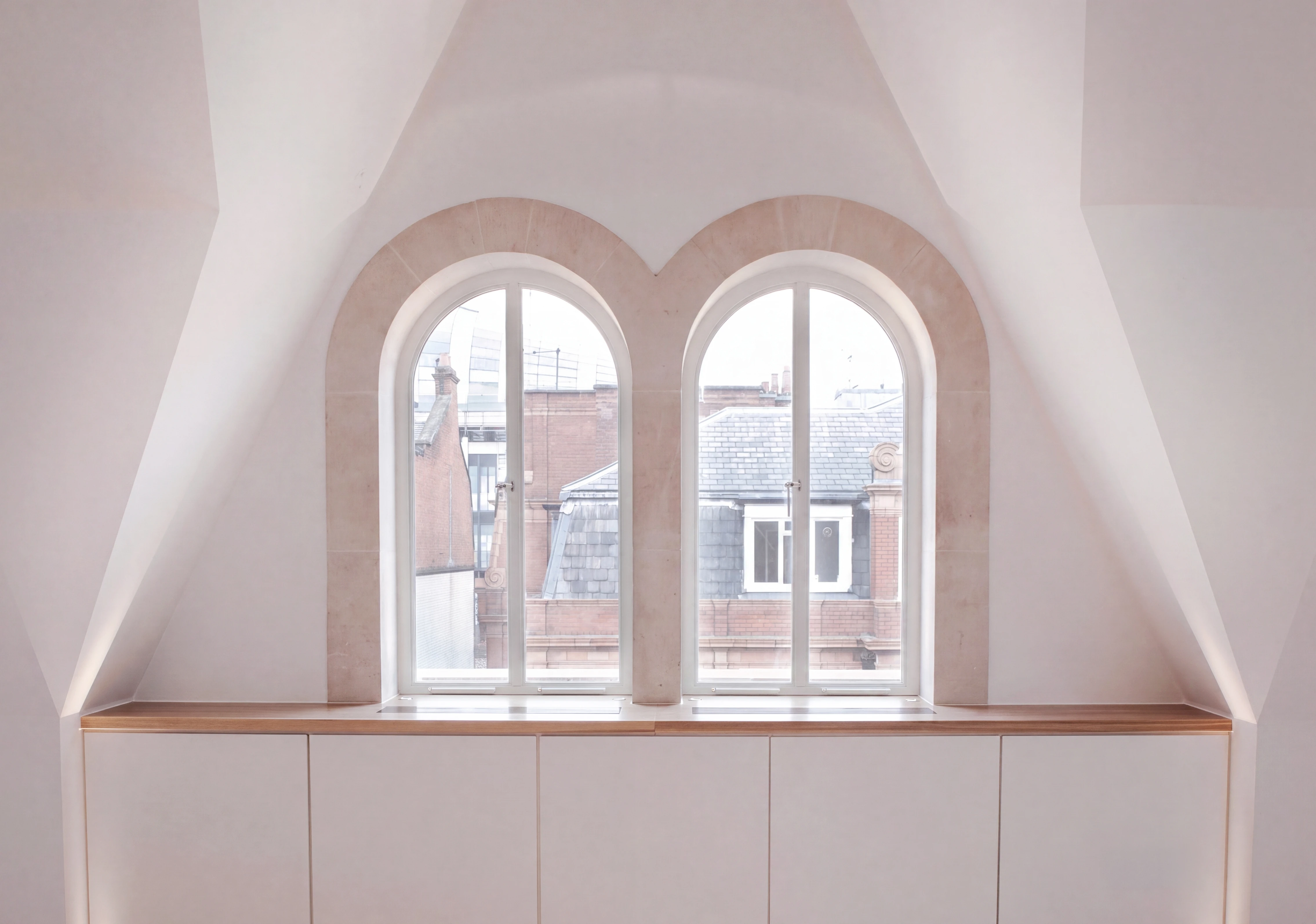 Attic room with paired arched windows in a stone surround, above built-in cabinetry with an oak top